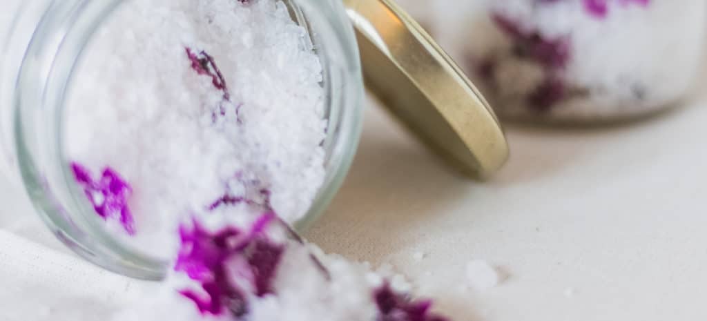 open jar of white bath salt with magenta flowers