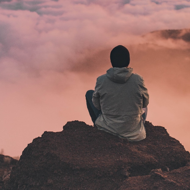 person sitting on high rock looking out at clouds