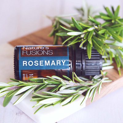 rosemary essential oil bottle lying on small cutting board with the herb